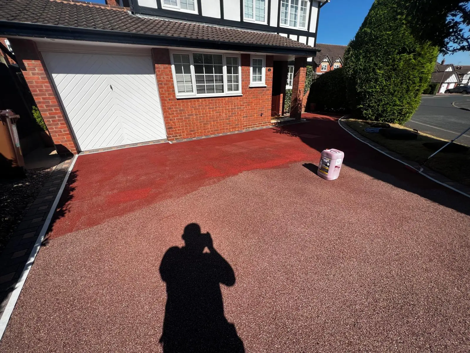 Red resin driveway mid-treatment showing faded original colour alongside freshly applied recolour