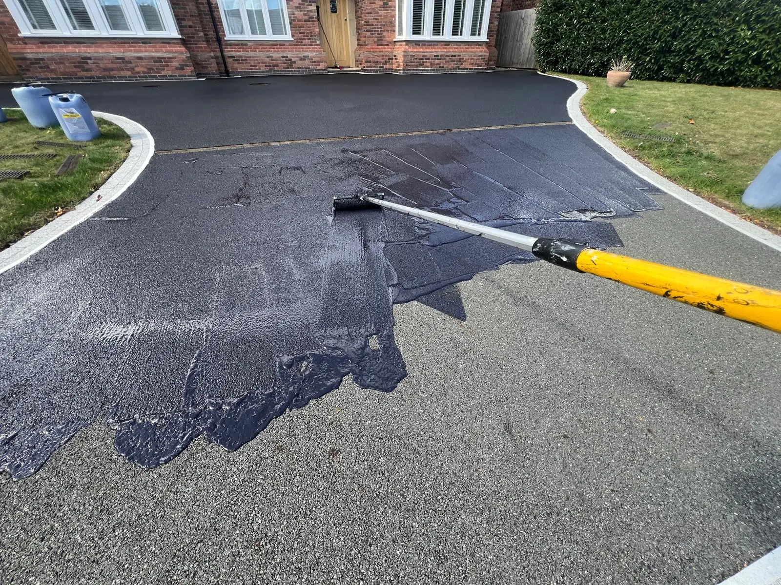 Large tarmac driveway mid-treatment showing faded grey alongside fresh jet black coating